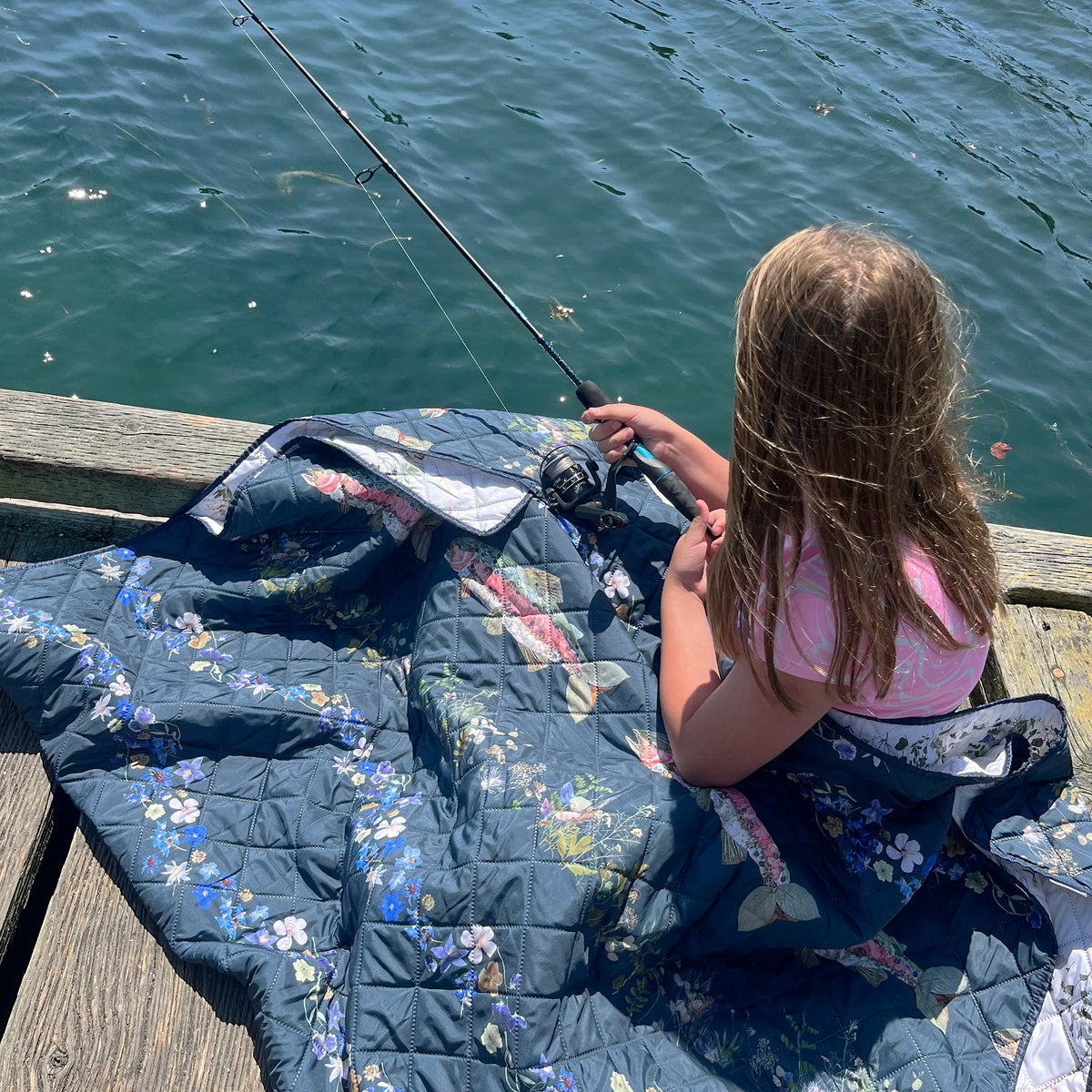 Child fishing on a dock with a pressed floral outdoor blanket on her legs