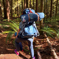 Person hiking in a forest with a rolled up pressed flower outdoor blanket on their back