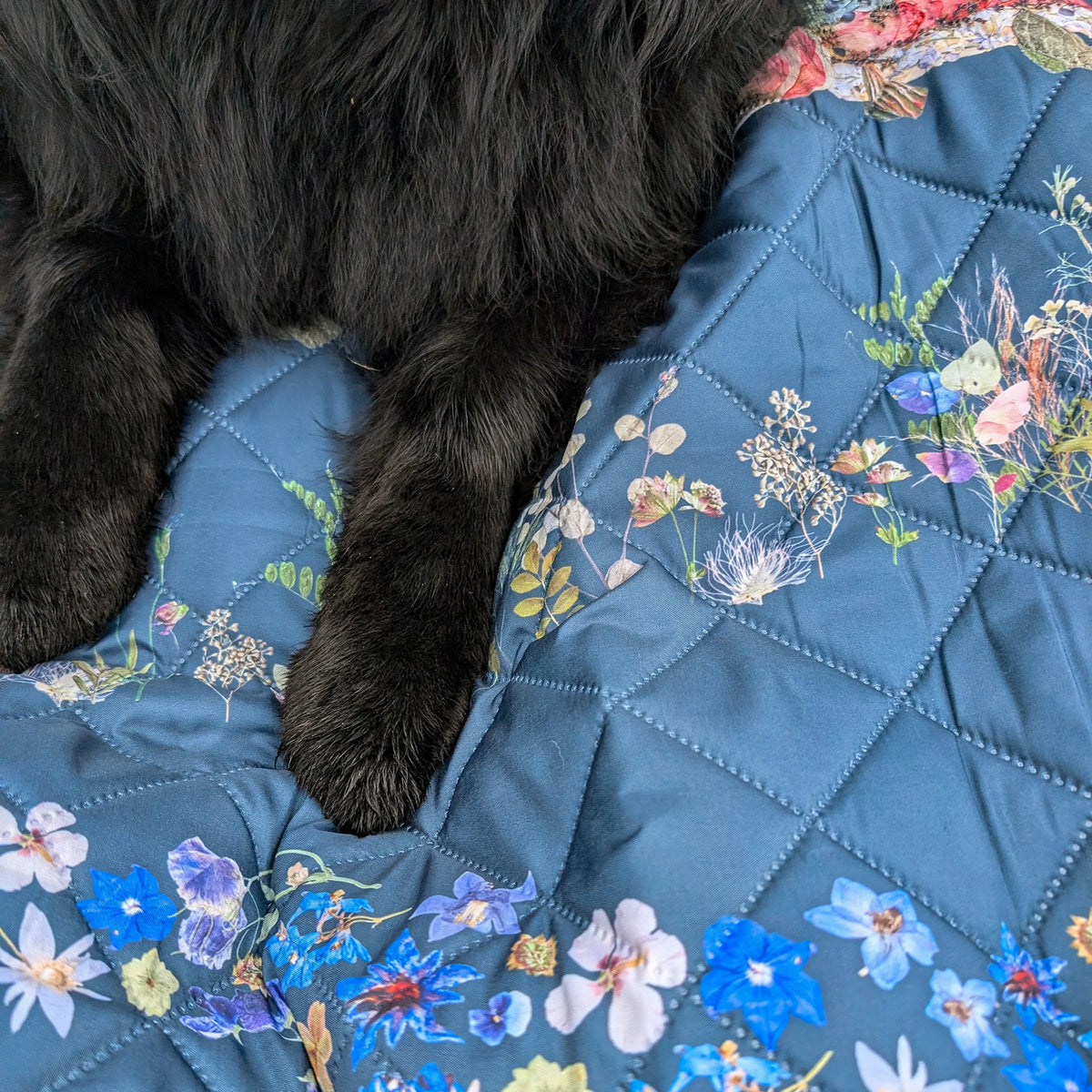 Floral-patterned waterproof outdoor quilt with a wet black dog lying on it