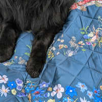 Floral-patterned waterproof outdoor quilt with a wet black dog lying on it