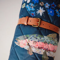 Floral-patterned picnic blanket with a fish design and brown leather strap.