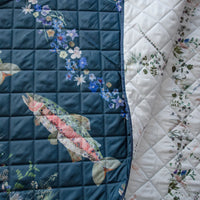 Two sides of an outdoor themed picnic blanket with floral and fish designs on a turquoise and white background.