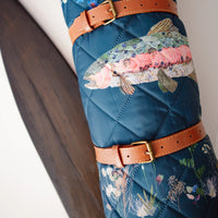 Turquoise quilted outdoor blanket with rainbow trout design and brown leather strap