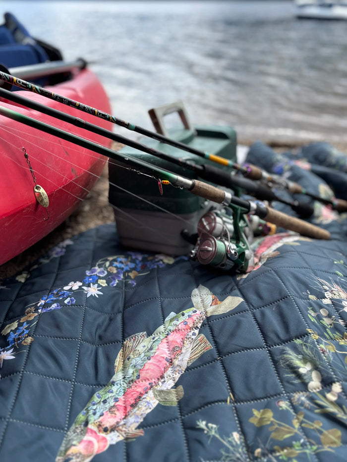 Fishing rods on a floral-patterned outdoor blanket with a kayak and water in the background