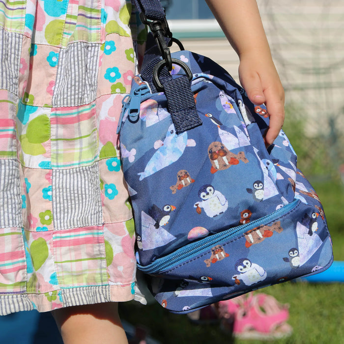 Child holding a blue lunch box with animal pattern outdoors