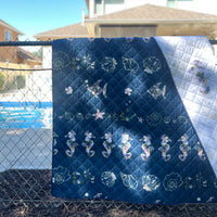 Coastal Drift Voyager Picnic Blanket hanging on a fence by a pool