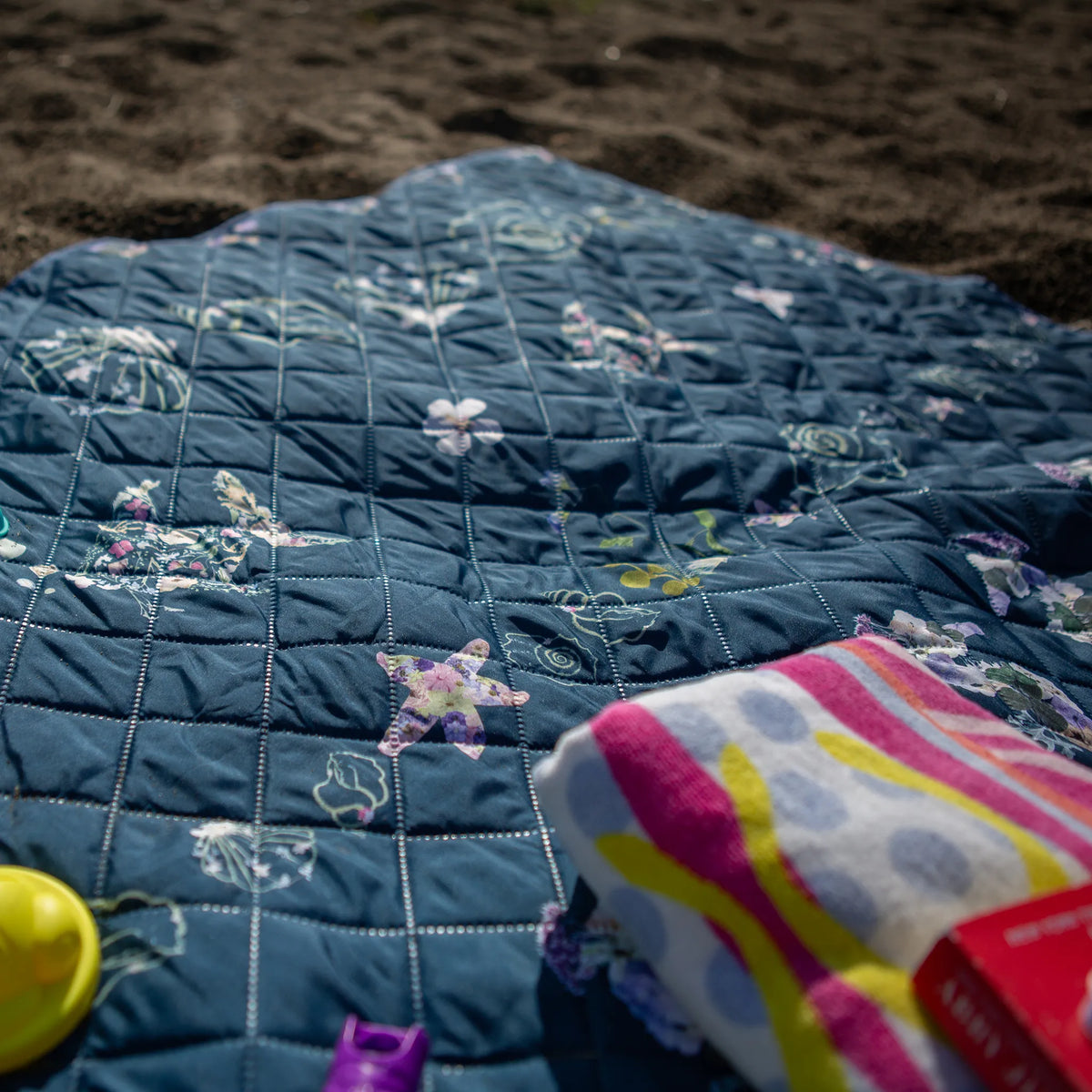 Blue quilt with floral patterns on a sandy surface