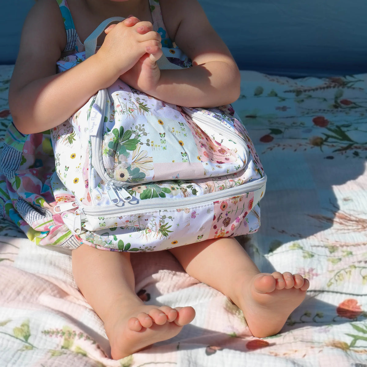 Child hugging patchwork floral lunch bag on a blanket outdoors