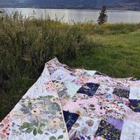 Double sided floral quilt on grass with a lake and mountains in the background