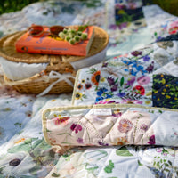 Floral Verona Picnic Blanket with a woven basket and books on a grassy outdoor setting