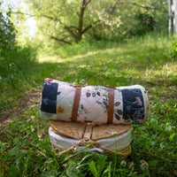 Rolled up picnic blanket by Oxeye Floral Co with picnic basked in outdoor grassy setting
