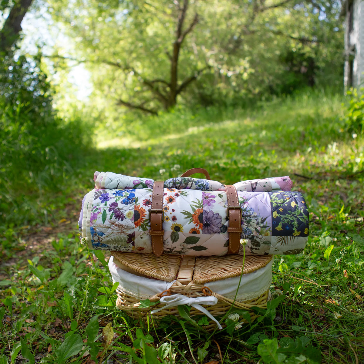 Verona Outdoor Voyager Blanket by Oxeye Floral Co rolled up with faux leather carry handle on a picnic basket