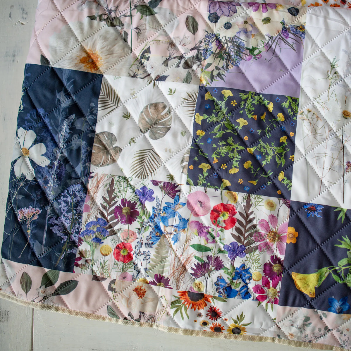 Outdoor Voyager blanket with patchwork flower design on a wooden surface.