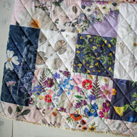 Outdoor Voyager blanket with patchwork flower design on a wooden surface.
