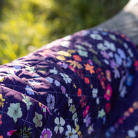 Floral-patterned quilted picnic blanket with a blurred nature background
