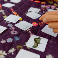 A close-up of a hand placing a white card  from a memory game onto a purple quilted fabric surface.