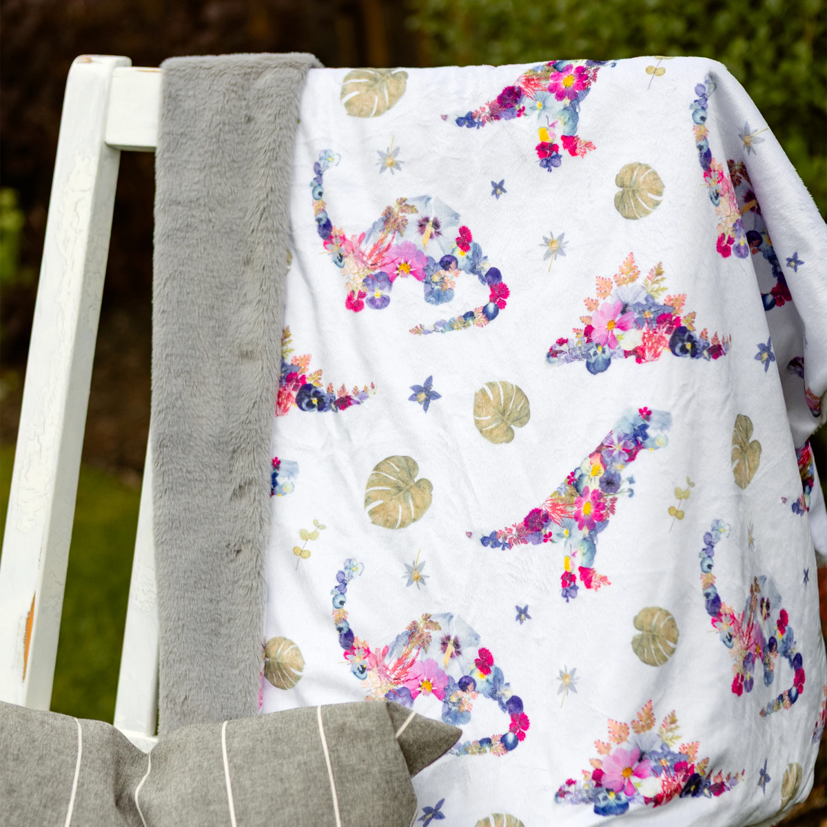 Pressed flower dinosaur minky baby blanket with plush grey backing draped on a chair outdoors.