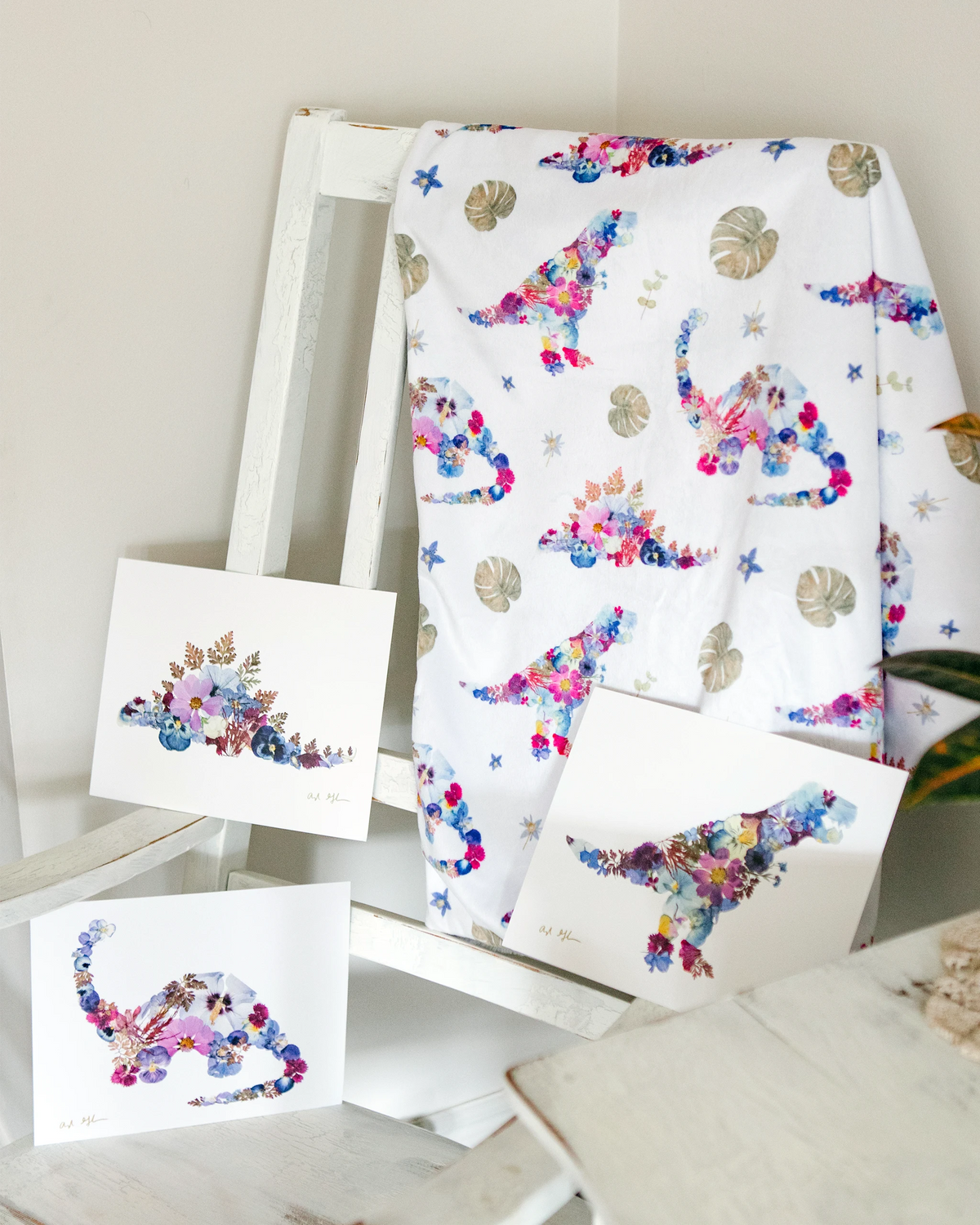 Pressed flower dinosaur baby blanket hanging on a chair with three matching dinosaur floral prints.