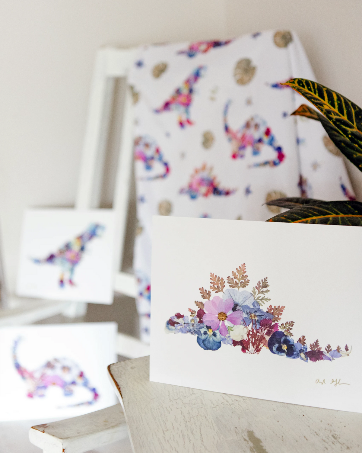 Art print of stegosaurus dino made out of pressed flowers, with matching baby blanket and other prints in the background.
