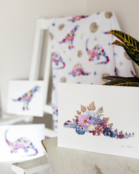 Art print of stegosaurus dino made out of pressed flowers, with matching baby blanket and other prints in the background.