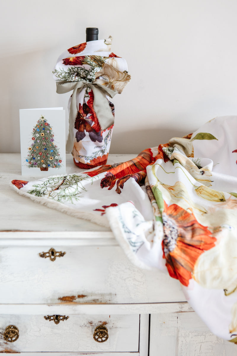 Decorative flower-patterned textiles and blankets on a white wooden surface with a Christmas card in the background.