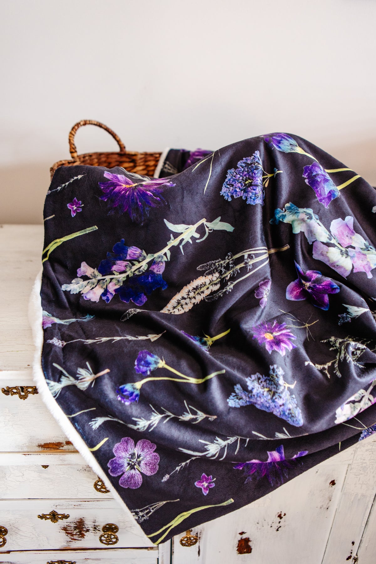 Floral-patterned blanket on a wooden surface with a wicker basket in the background