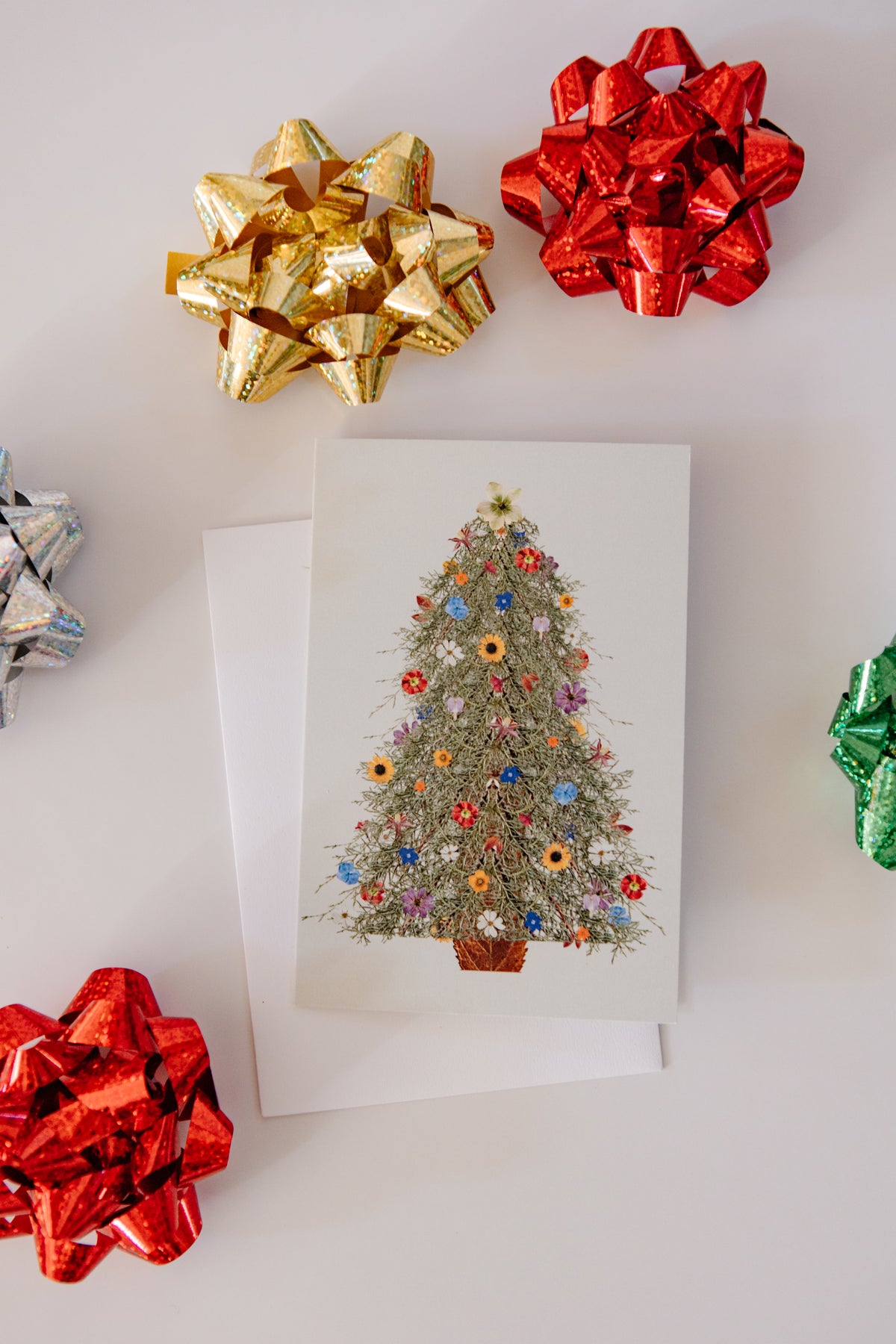 Decorative greeting card with a Christmas tree design surrounded by colorful bows on a white background