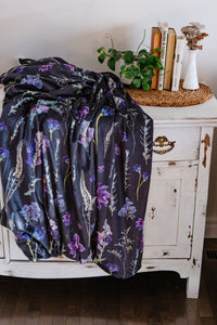 Pressed floral-patterned blanket draped over a white cabinet with books and a plant on top.