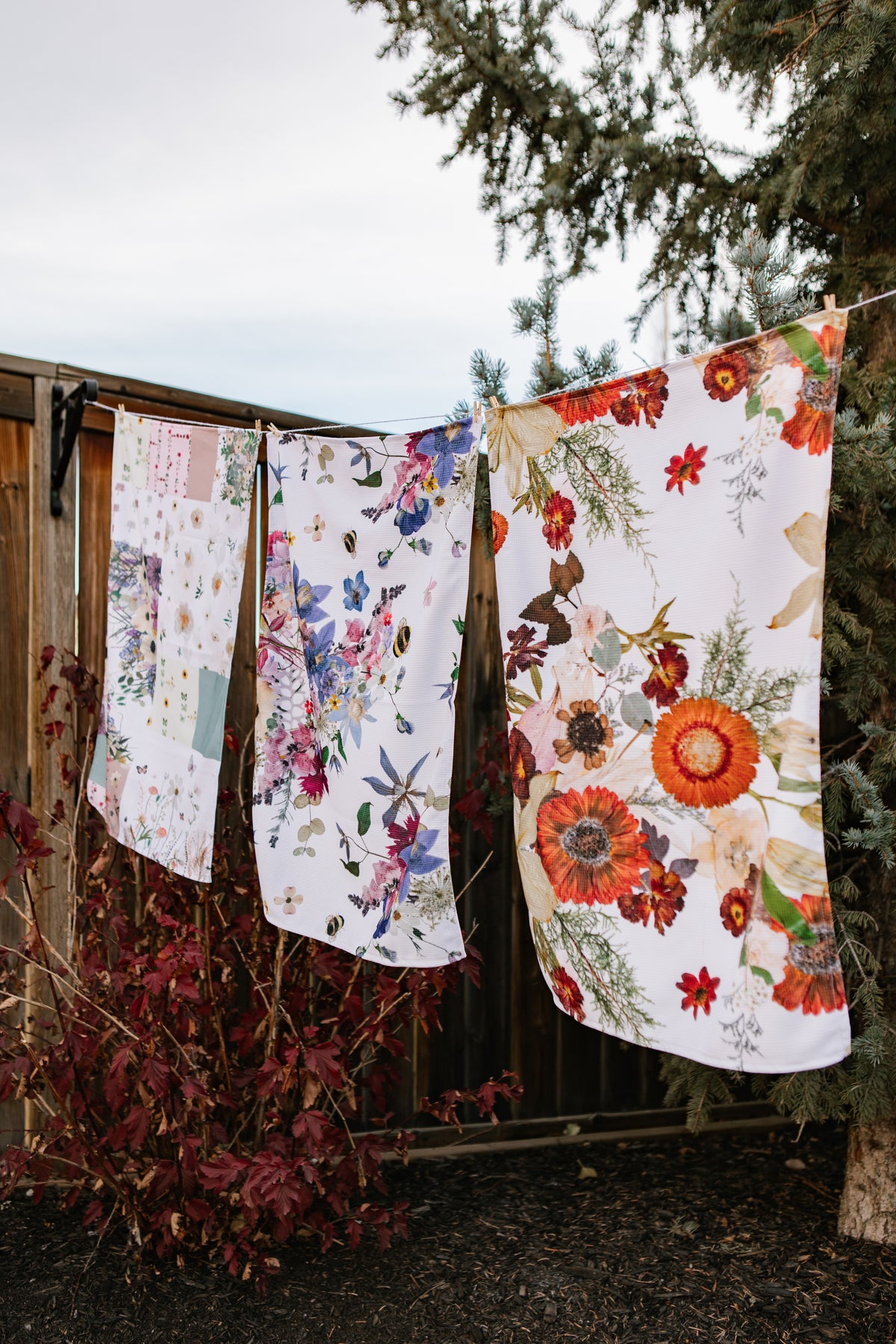 Floral-patterned towels hanging on a line outdoors with trees in the background.