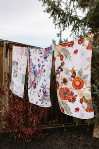 Floral-patterned towels hanging on a line outdoors with trees in the background.
