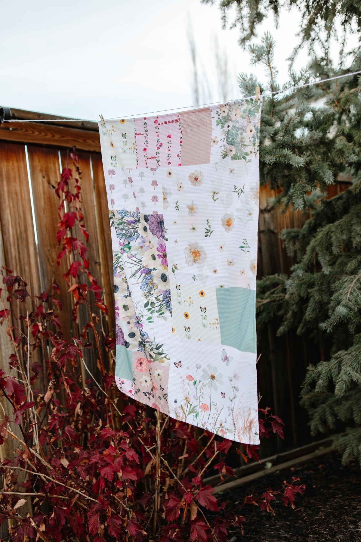 Floral patchwork tea towel hanging outdoors with trees and branches in the background