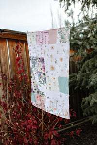 Floral patchwork tea towel hanging outdoors with trees and branches in the background