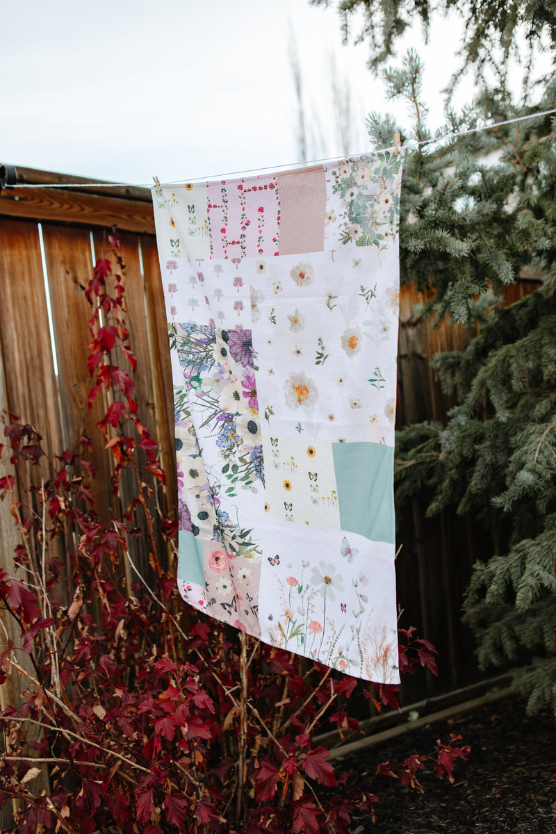 Floral patchwork tea towel hanging outdoors with trees and branches in the background