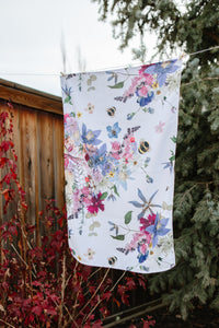 Flowery tea towel with a wooden fence and trees in the background.