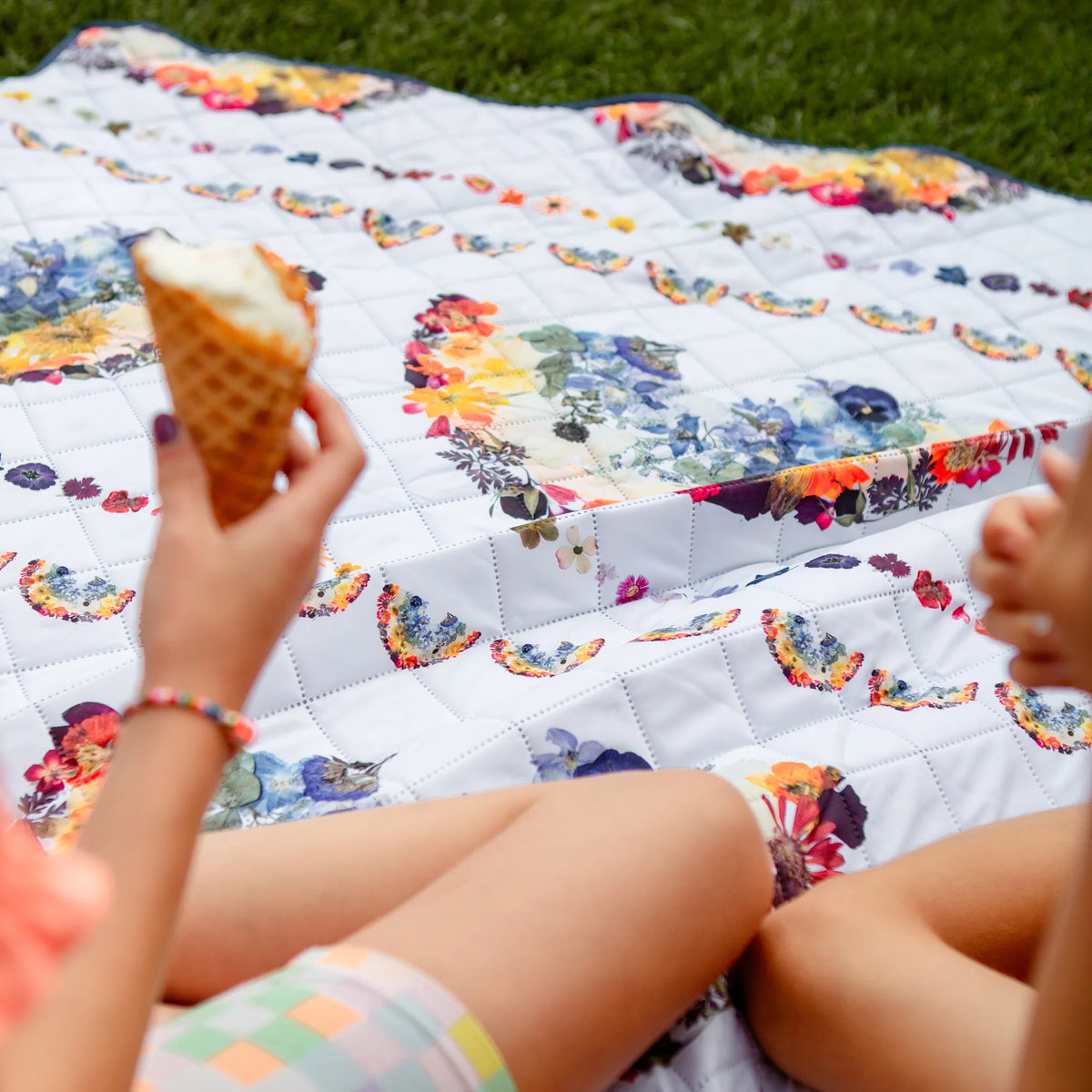 Person holding an ice cream cone on a floral rainbow blanket outdoors