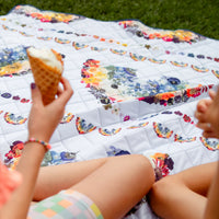 Person holding an ice cream cone on a floral rainbow blanket outdoors