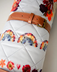 Rolled up floral-patterned blanket with rainbow designs and a brown strap.