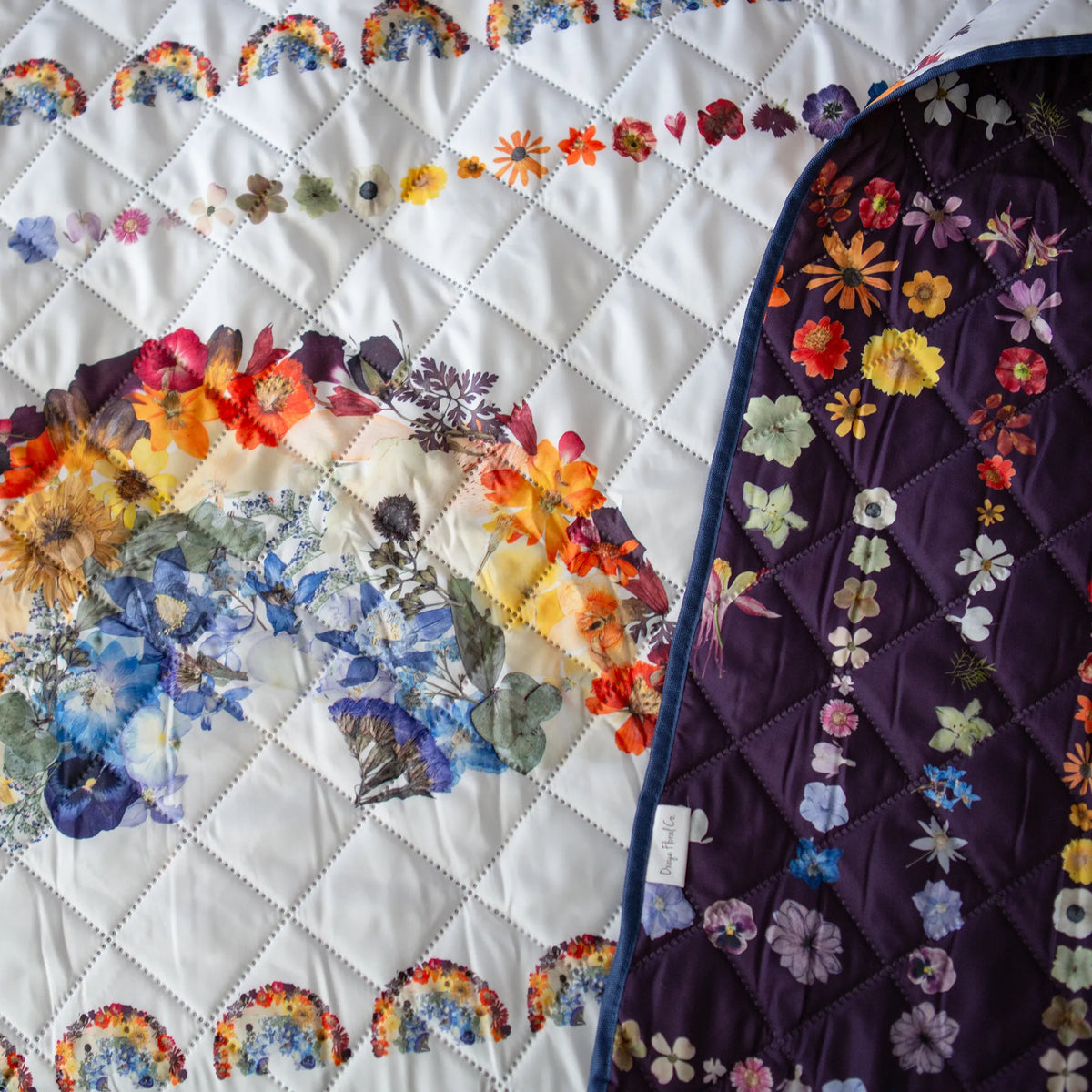Quilted picnic blanket with floral and rainbow patterns on a white background