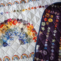 Quilted picnic blanket with floral and rainbow patterns on a white background