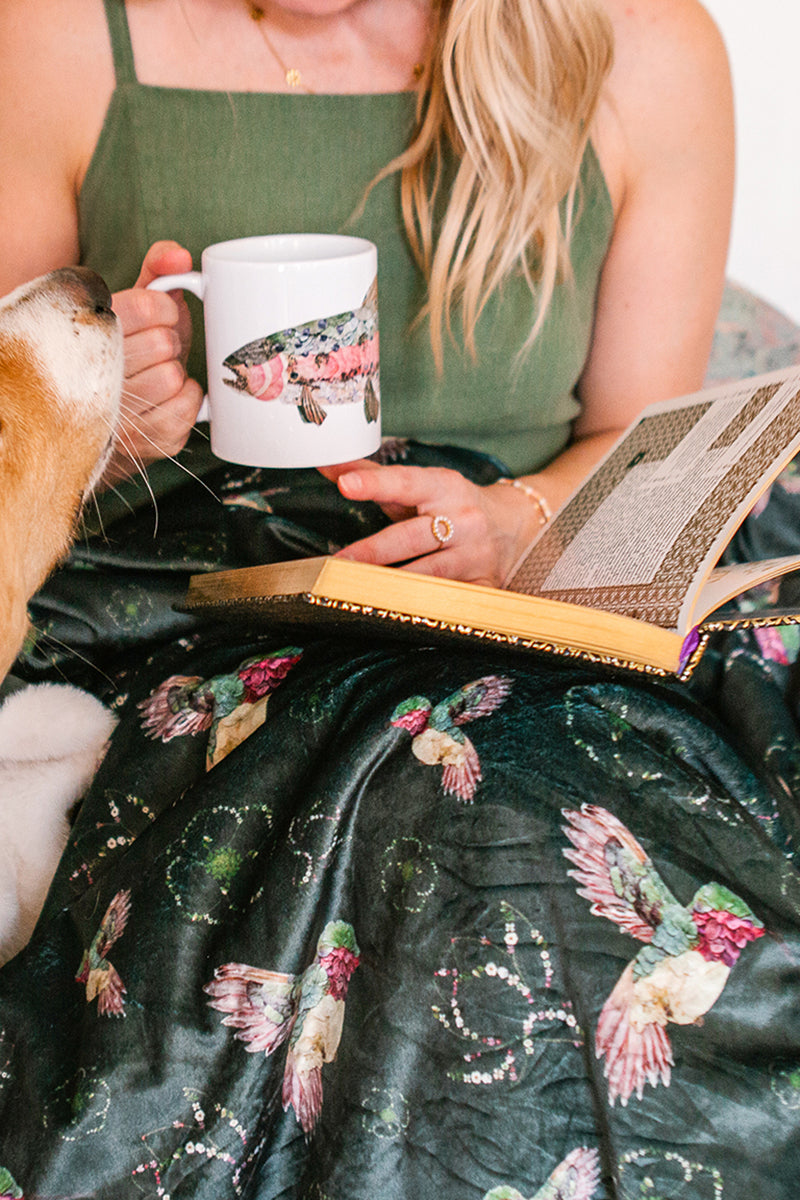 Woman holding a fish-themed mug with a floral hummingbird blanket