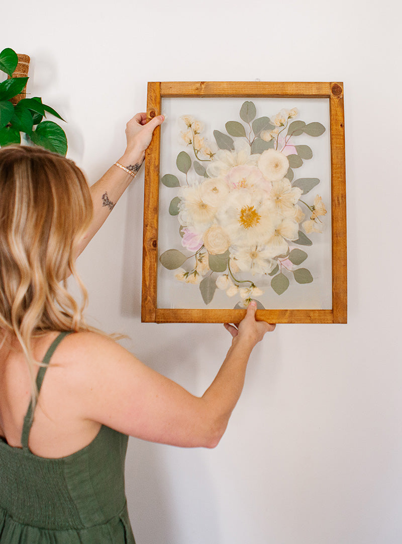 Woman hanging a framed pressed bridal bouquet keepsake by Oxeye Floral Co.