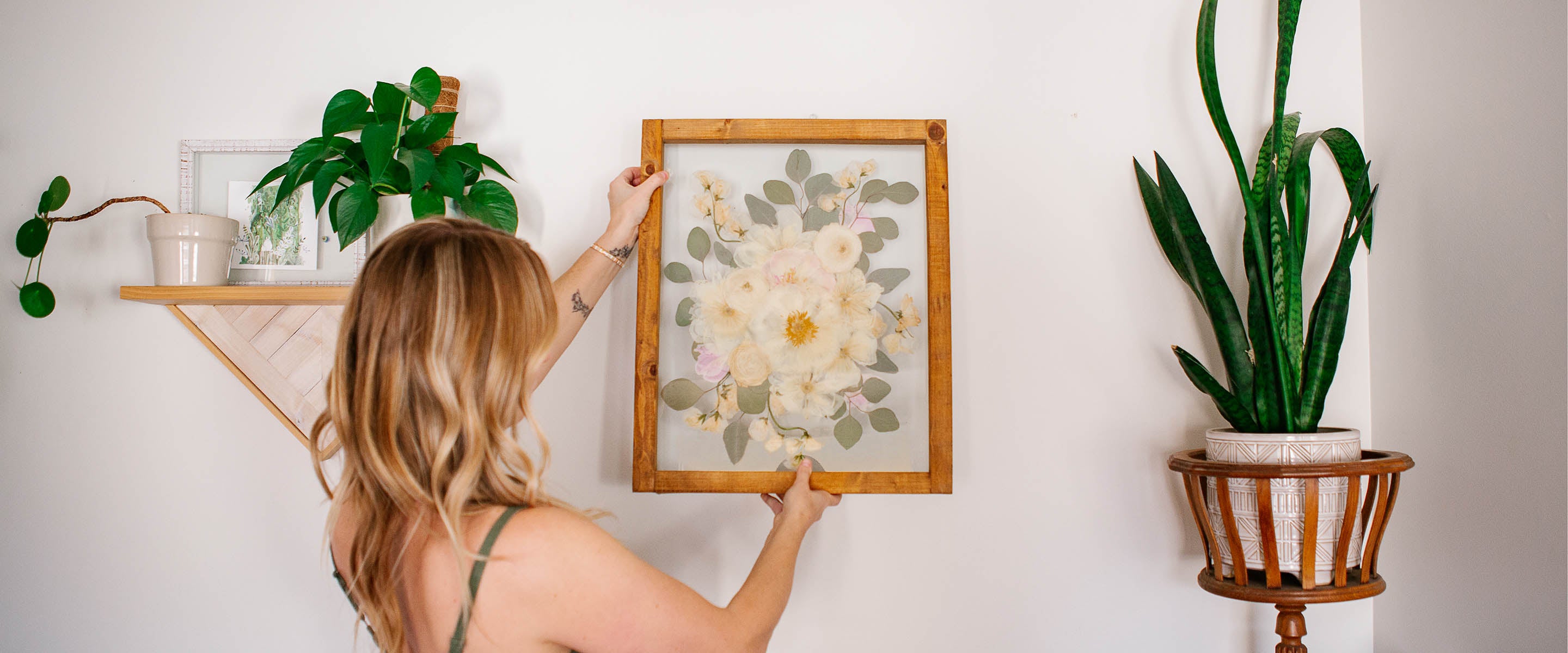 Woman hanging a framed pressed bridal bouquet keepsake by Oxeye Floral Co.