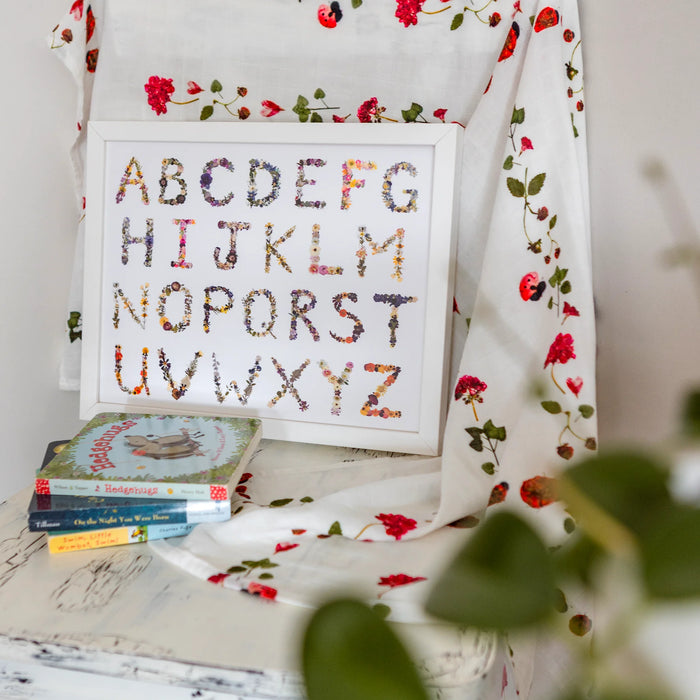 Floral alphabet chart on a floral-patterned blanket with books underneath