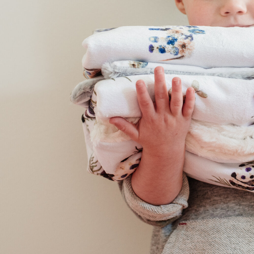 Child holding a stack of Oxeye Floral Co baby blankets