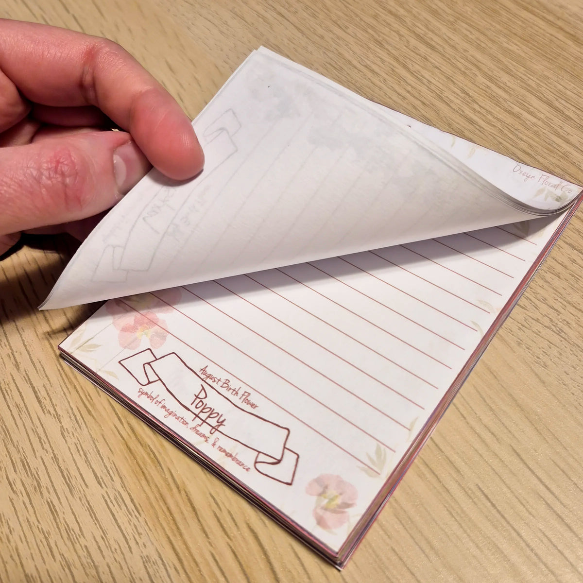 Hand holding a small notebook with lined pages on a wooden surface