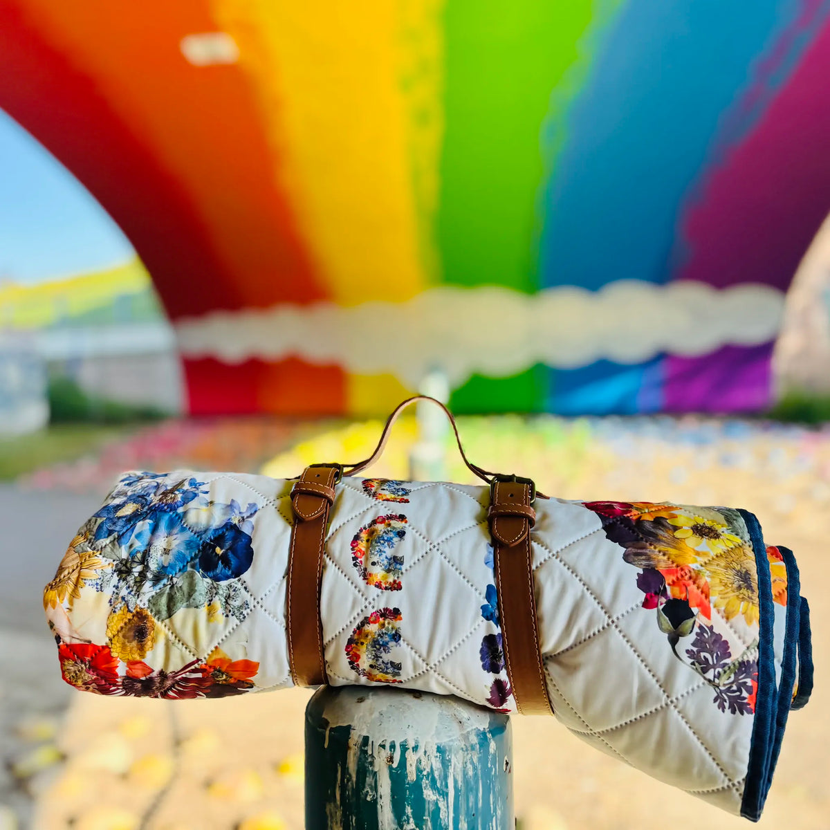 Floral-patterned picnic blanket with brown straps against a colourful mural background