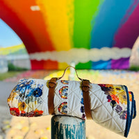 Floral-patterned picnic blanket with brown straps against a colourful mural background
