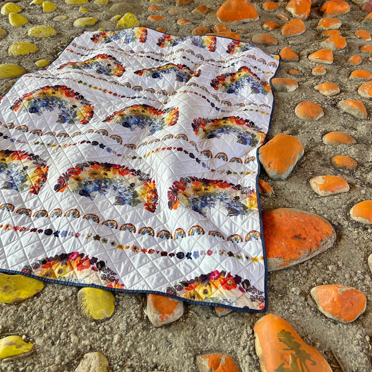 Quilted picnic blanket with floral rainbow patterns on a stone surface