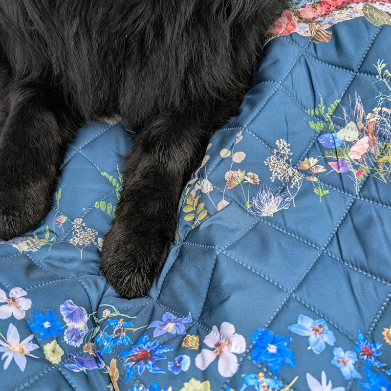 Floral-patterned waterproof outdoor quilt with a wet black dog lying on it