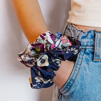 Multicolored floral scrunchies held by a person wearing blue jeans.